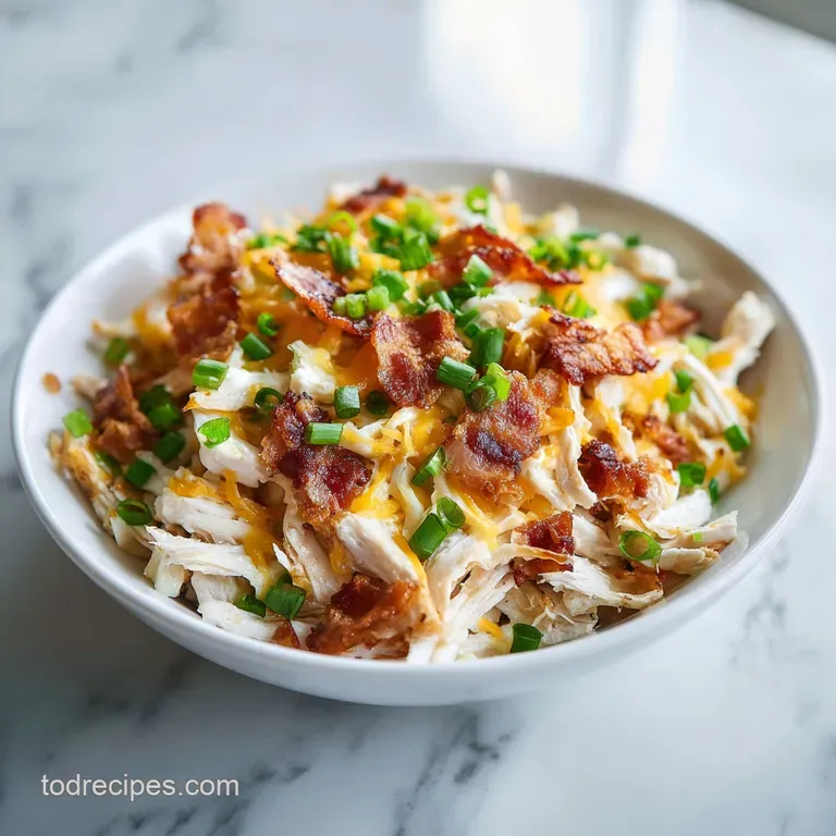 Shredded chicken in a creamy sauce served in a white ceramic bowl, topped with golden bacon and fresh green onions.